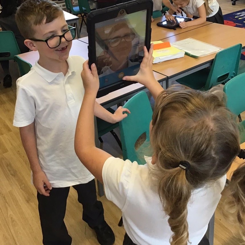 A girl taking a picture of a boy on a tablet
