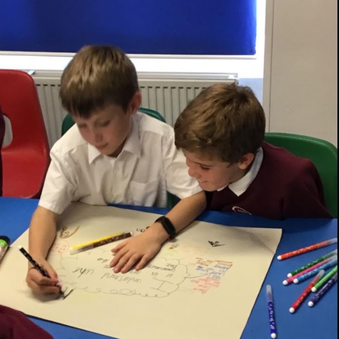 Two boys working together to write on a large piece of paper