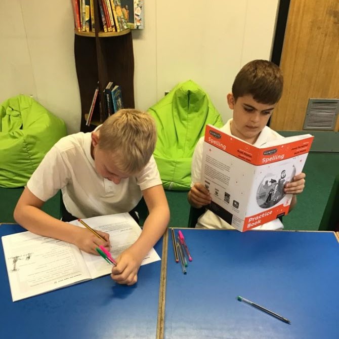 A boy writing in a book, another reading a book