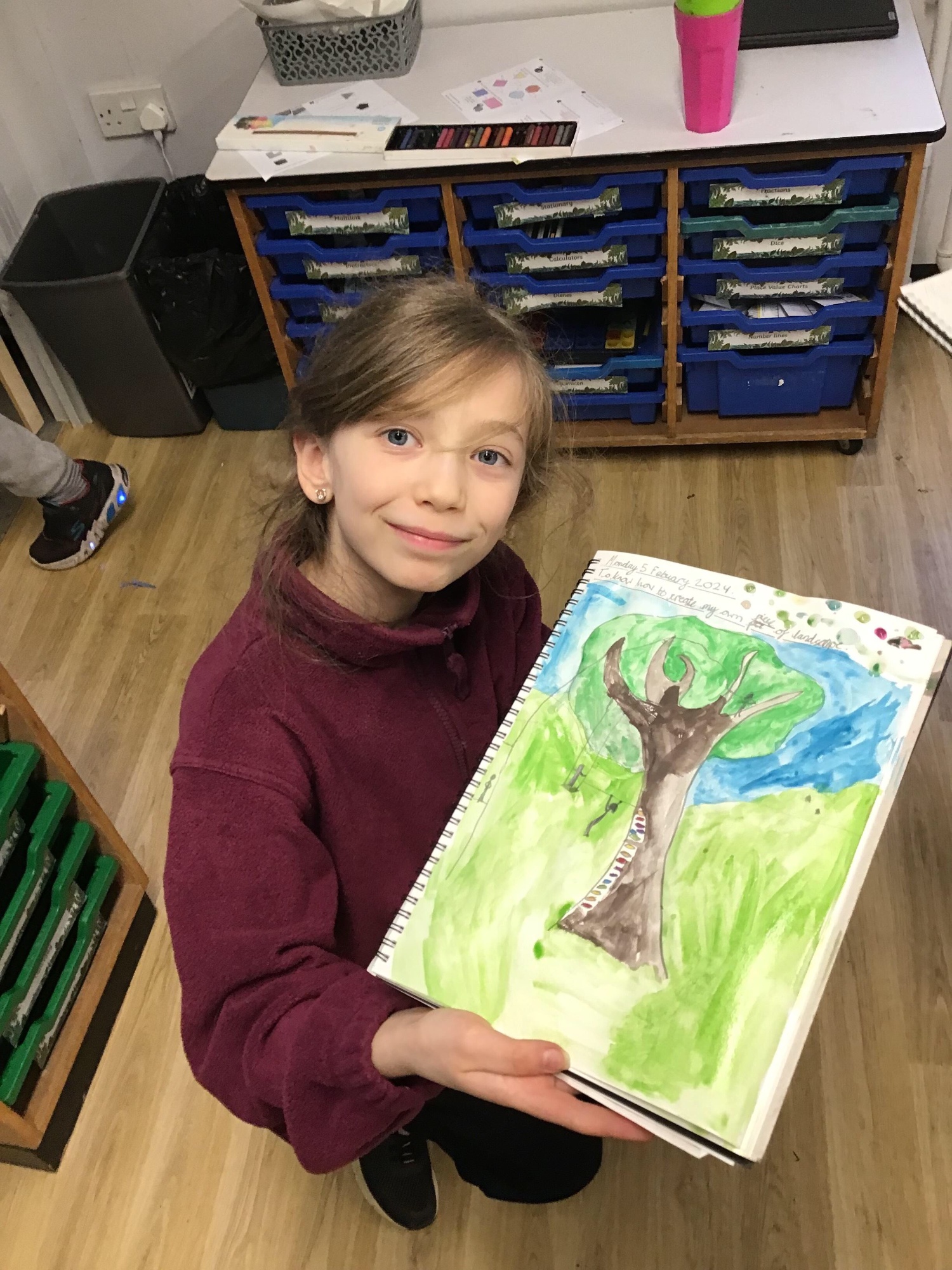 A smiling girl showing her painting of a tree