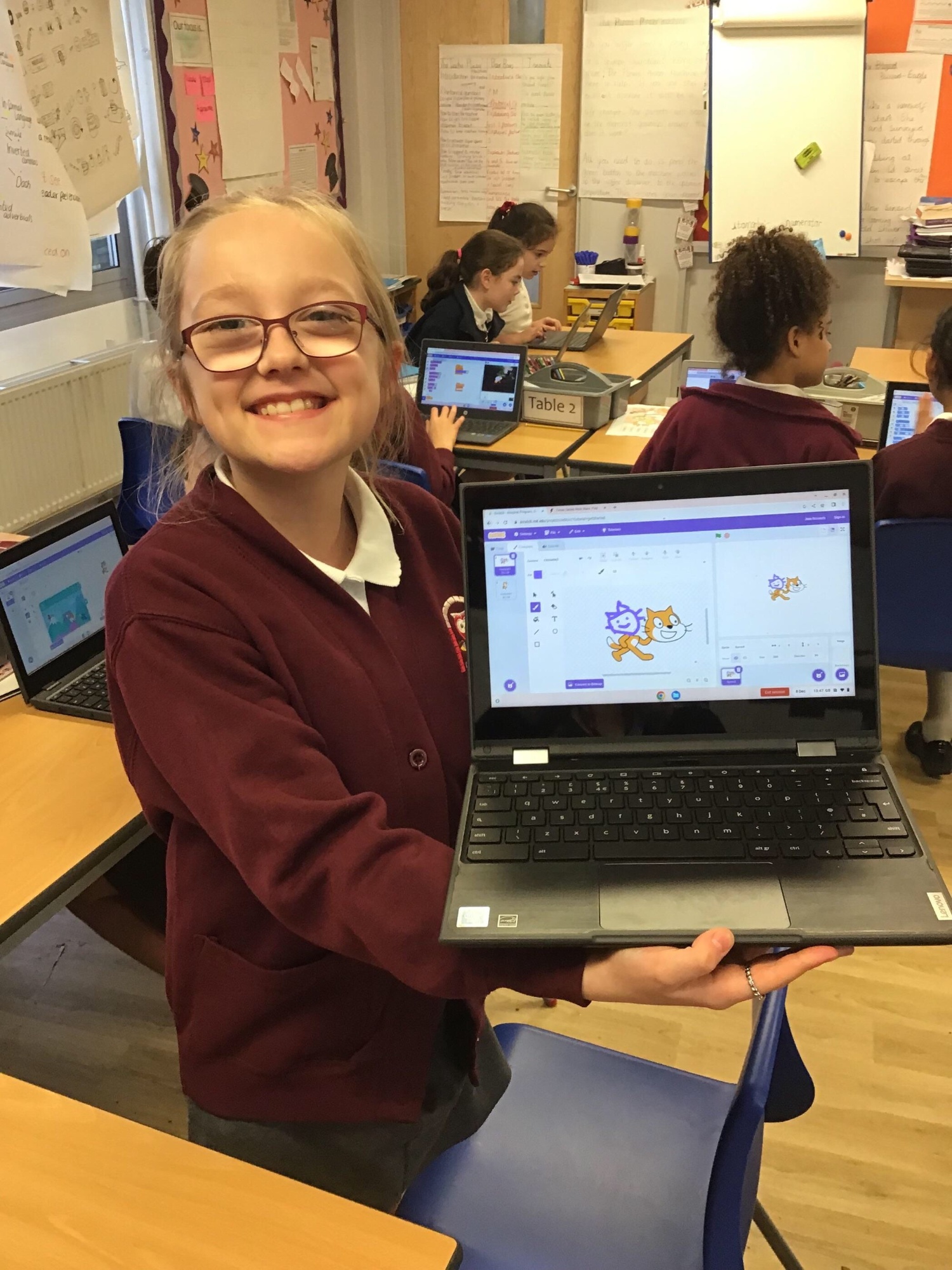 A smiling girl showing her work on a laptop