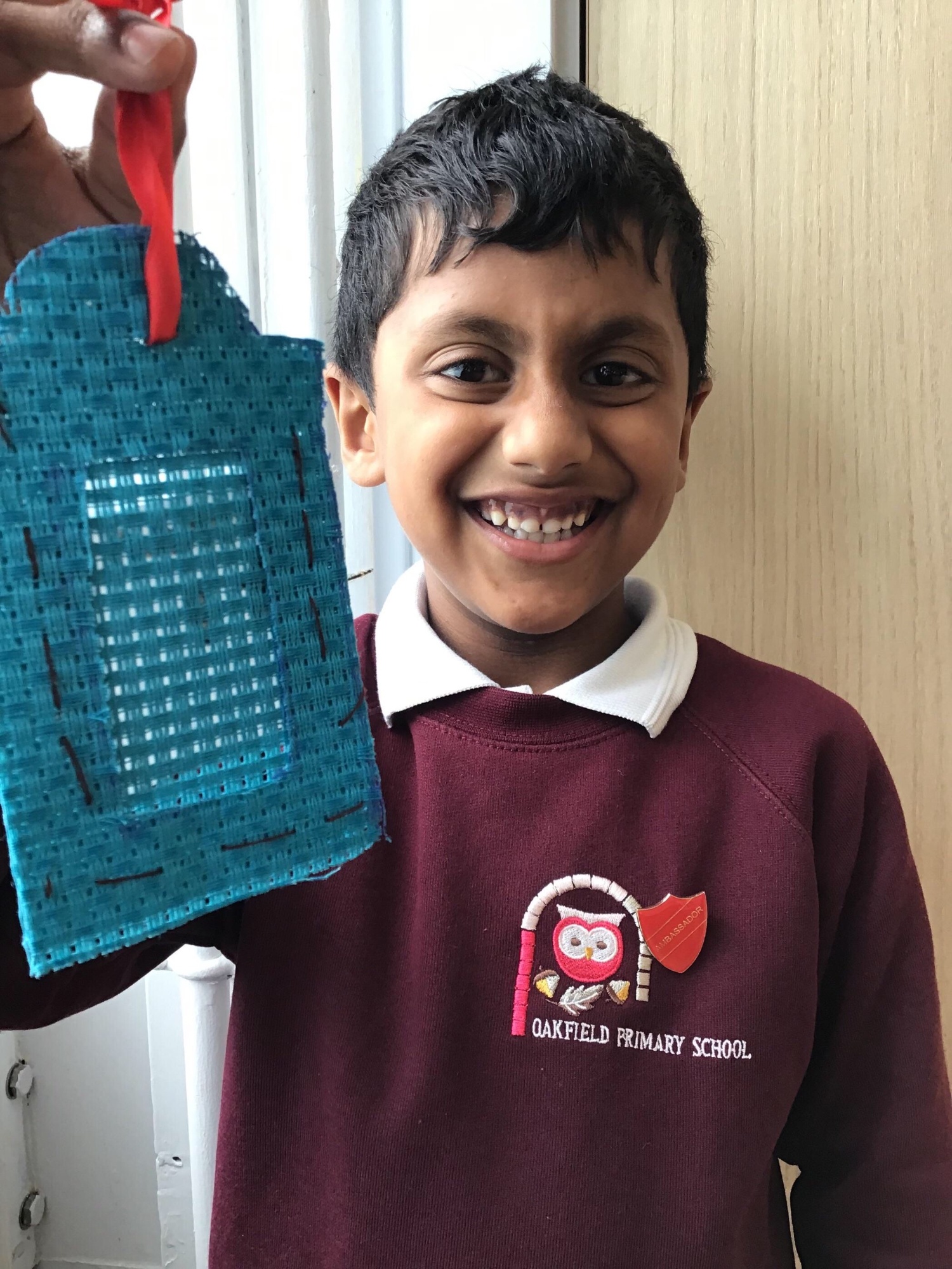 A smiling boy holding a luggage tag he has sewn